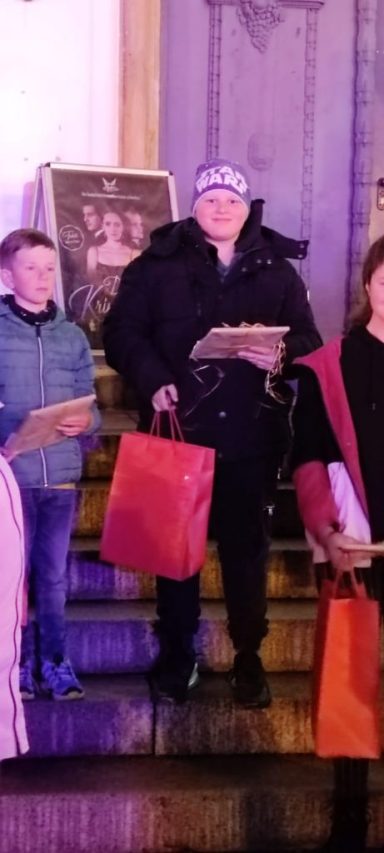 Ein Mann mit roter Tüte steht mit Kindern und Erwachsenen auf einer Treppe.