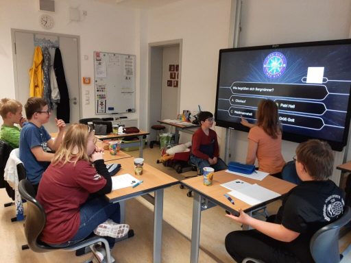 Gruppe von Kindern in einem Klassenraum schaut auf eine Präsentation an einem Bildschirm.