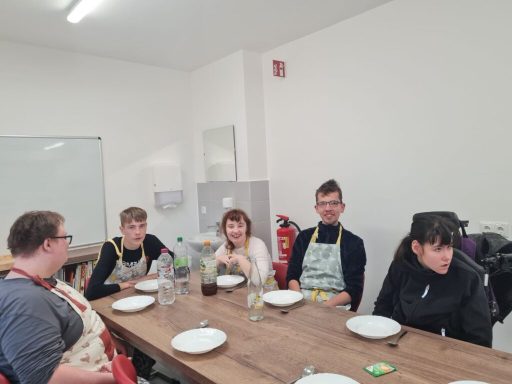 Fünf Personen sitzen an einem Tisch mit leeren Tellern in einem Küchenbereich.