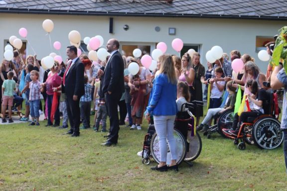 Menschenmenge mit Luftballons, einige Kinder in Rollstühlen, festliche Stimmung im Freien.