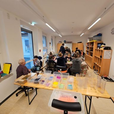 Gruppenschüler arbeiten an einem Tisch mit bunten Materialien in einem hellen Raum.