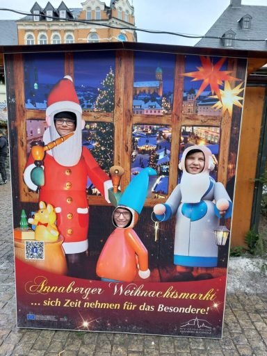 Drei Personen in Weihnachtskostümen vor einer festlich geschmückten Fensterfront.