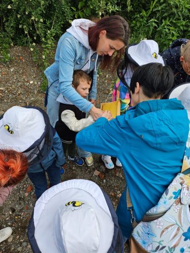 Eine Gruppe von Kindern mit weißen Hüten um eine erwachsene Person, die ihnen etwas zeigt.