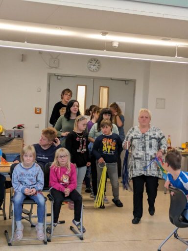 Gruppe von Kindern und Erwachsenen in einem hellen Raum, versammelt in einer Reihe.