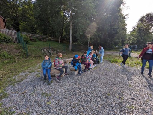 Auf einer Kiesfläche sitzen mehrere Kinder in bequemer Kleidung und lachen.