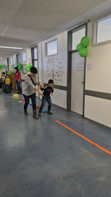 Kinder gehen in einem Flur mit bunten Ballons und farbigen Linien auf dem Boden.