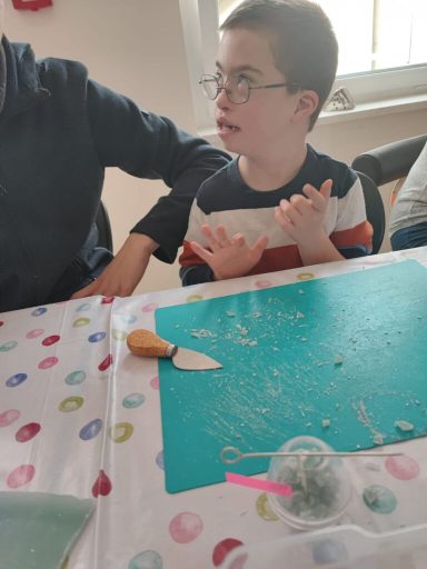 Ein Junge mit Brille sitzt an einem Tisch mit Bastelmaterialien und einer Klinge.