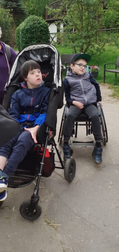 Zwei Kinder, eines im Rollstuhl und das andere im Kinderwagen, schauen nach vorne.