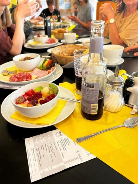 Frühstückstisch mit verschiedenen Speisen, inklusive Obst, Fleisch und Getränken.