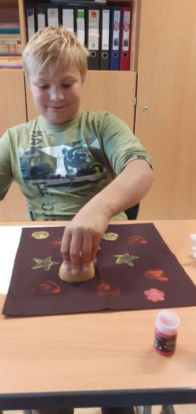 Ein Junge färbt mit Schwamm und Farbe auf einer Tischunterlage mit bunten Blättern.