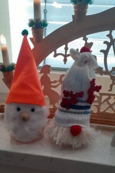 Zwei Weihnachtsmänner aus Bastelmaterial, einer mit orangefarbener Mütze, der andere mit rotem Bommel.