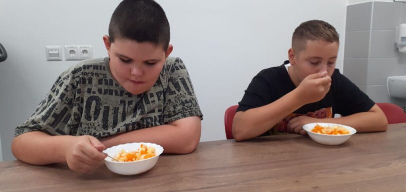 Zwei Jungen sitzen an einem Tisch und essen aus weißen Schalen.