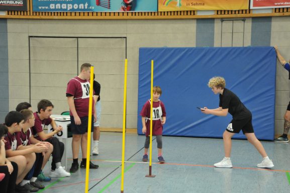 Junge trainiert mit einem Trainer, während andere Spieler in der Halle zuschauen.
