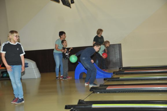Kinder und Erwachsene spielen Bowling in einer Hallenumgebung.