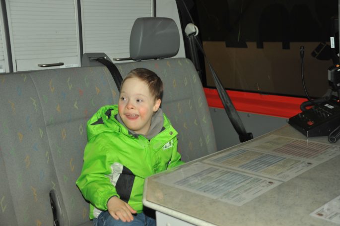 Ein fröhlicher Junge in einer grünen Jacke sitzt in einem Fahrzeug.