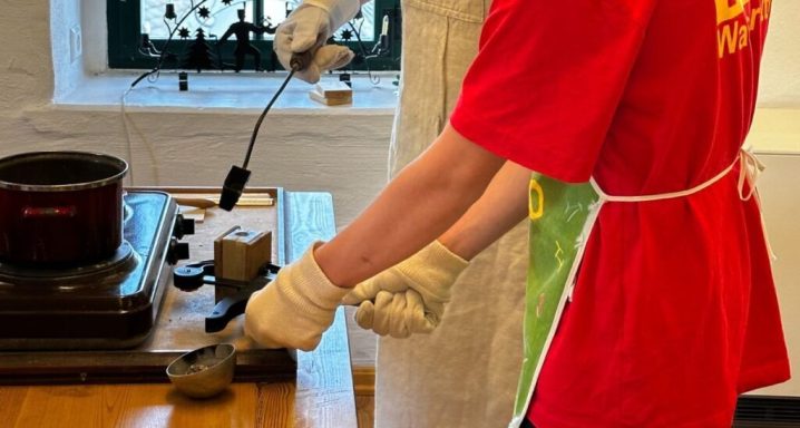 Person in rotem Shirt und Schürze hantiert mit Werkzeugen in einer Werkstatt.