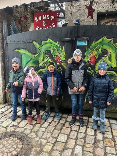 Fünf Kinder stehen vor einer Wand mit grünen Drachenmalereien.