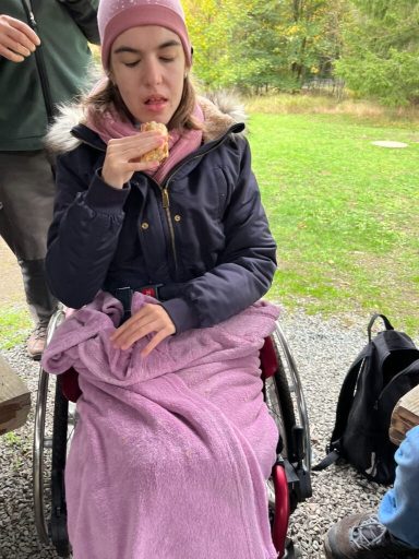 Eine junge Frau im Rollstuhl mit einer Decke, die einen Snack isst.