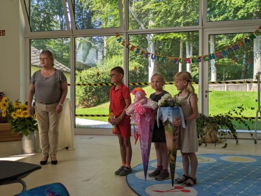 Drei Kinder halten große bunte Regenschirme, während eine Erwachsene daneben steht.