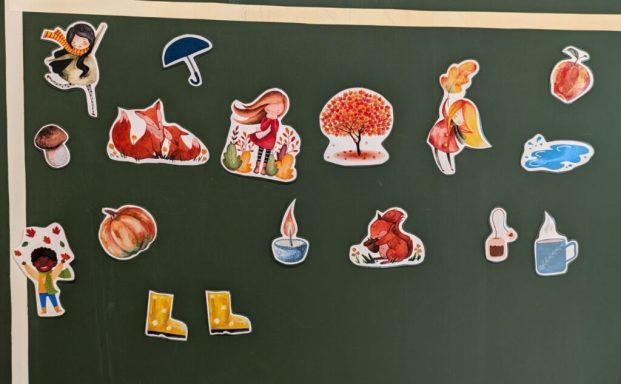 Bunte Sticker mit Tieren, Pflanzen und Alltagsgegenständen auf einer Tafel.