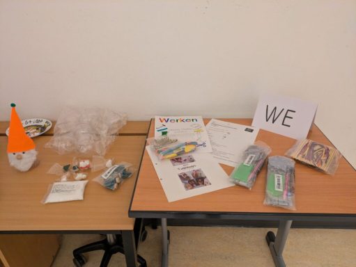 Tisch mit Bastelmaterialien, Papier, Stiften und einem Schild mit der Aufschrift „WE“.