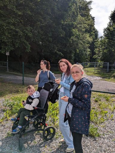 Drei Frauen und ein Junge im Rollstuhl stehen an einem Waldweg.