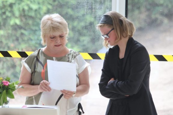 Zwei Frauen betrachten Dokumente, eine steht und spricht, die andere hört aufmerksam zu.
