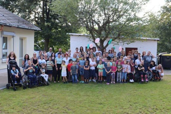Gruppenbild von etwa 50 Personen im Freien, umgeben von Bäumen und einem Gebäude.