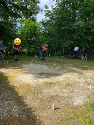 Gruppenspiel im Freien, Menschen mit einem großen Ball und Holzstäben auf einer Wiese.