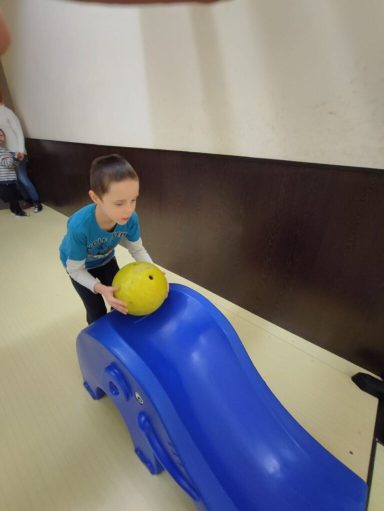 Ein Junge rollt eine gelbe Bowlingkugel auf einer blauen Rutsche.
