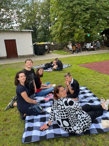 Gruppe von Menschen in einem Park, sitzend auf einer Decke, entspannt und unterhaltend.