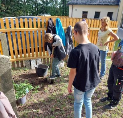 Kinder pflanzen gemeinsam im Garten, während eine Person mit einer Schaufel arbeitet.