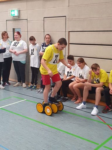 Ein Junge steht auf einer rollenden Plattform, umgeben von Zuschauern in weißen T-Shirts.