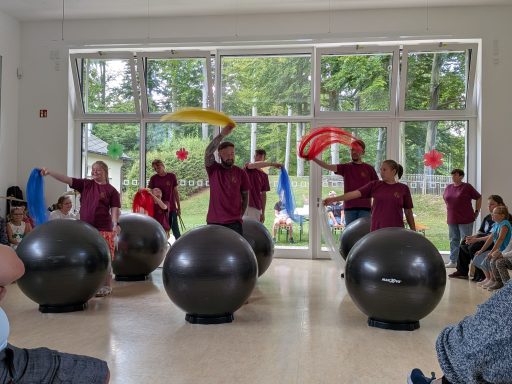 Gruppe von Personen in Rot mit großen Bällen und bunten Tüchern während einer Aufführung.