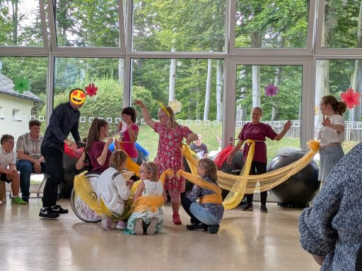 Gruppenvorführung mit bunten Stoffen und fröhlichen Teilnehmern in festlicher Atmosphäre.