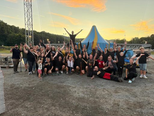 Gruppe von Menschen in schwarzer Kleidung, die fröhlich vor einem Zelt posieren.