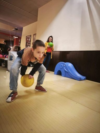 Ein Kind hebt einen Ball, während eine andere Person im Hintergrund mit einem Ball spielt.