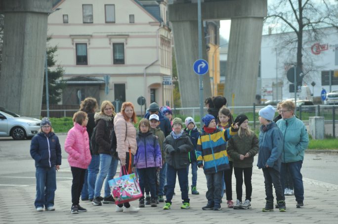 Gruppe von Kindern und Jugendlichen steht unter einer Brücke, umgeben von Gebäuden.