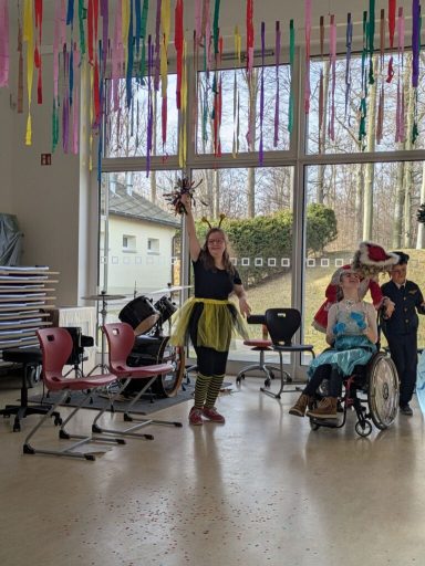 Frau in buntem Kostüm hebt die Hand, um mit anderen in einem hellen Raum zu feiern.