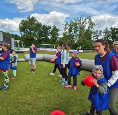 Kinder und Erwachsene in blauen Westen spielen im Freien mit roten Bällen.