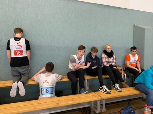 Jugendliche in Sportkleidung sitzen auf einer Bank in einer Halle.
