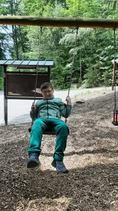 Ein Junge schwingt fröhlich auf einer Wippe im Wald.