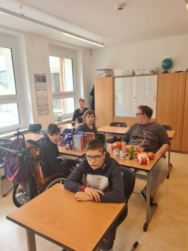 Schüler sitzen an Tischen in einem Klassenzimmer, einige essen Snacks und trinken.