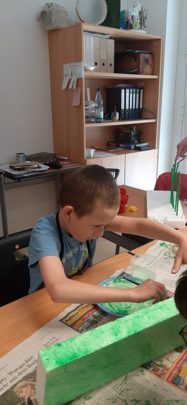 Junge sitzt an einem Tisch und arbeitet mit buntem Papier und Bastelmaterialien.