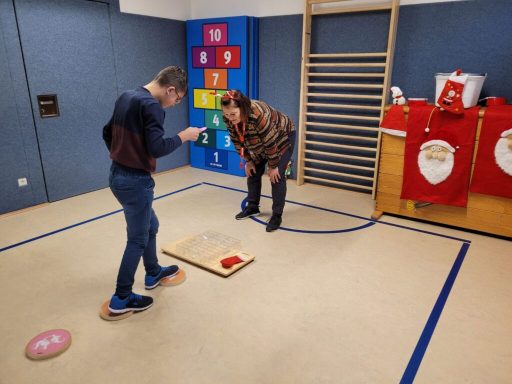 Zwei Personen in einem Raum, eine steht und schaut auf ein Brett, die andere kniet daneben.