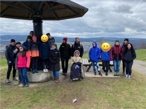 Gruppenausflug mit Menschen in bunten Jacken unter einem Pavillon in der Natur.