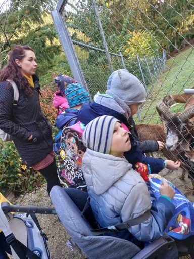 Eine Frau steht neben zwei Kindern, die Futtertiere an einer Hütte füttern.