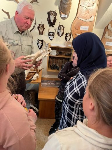 Mann zeigt Tierknochen einer Gruppe von Schülerinnen und Schülern in einem Museum.
