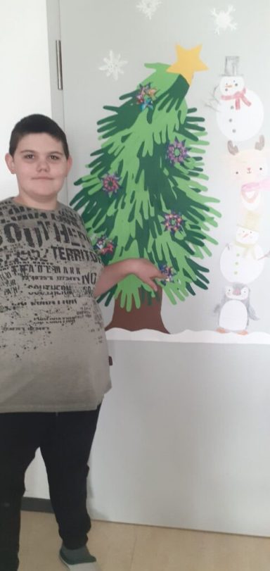 Ein Junge steht neben einem bunten Weihnachtsbaum und einer Schneemann-Dekoration.