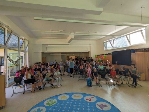 Gruppenevent in einem hellen Raum mit vielen Menschen, Stühlen und einer großen Leinwand.